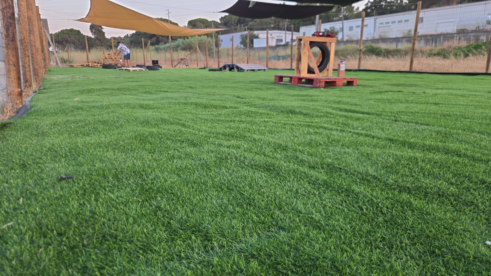 Parque exterior do DogVilla com relva e equipamento de agility para cães
